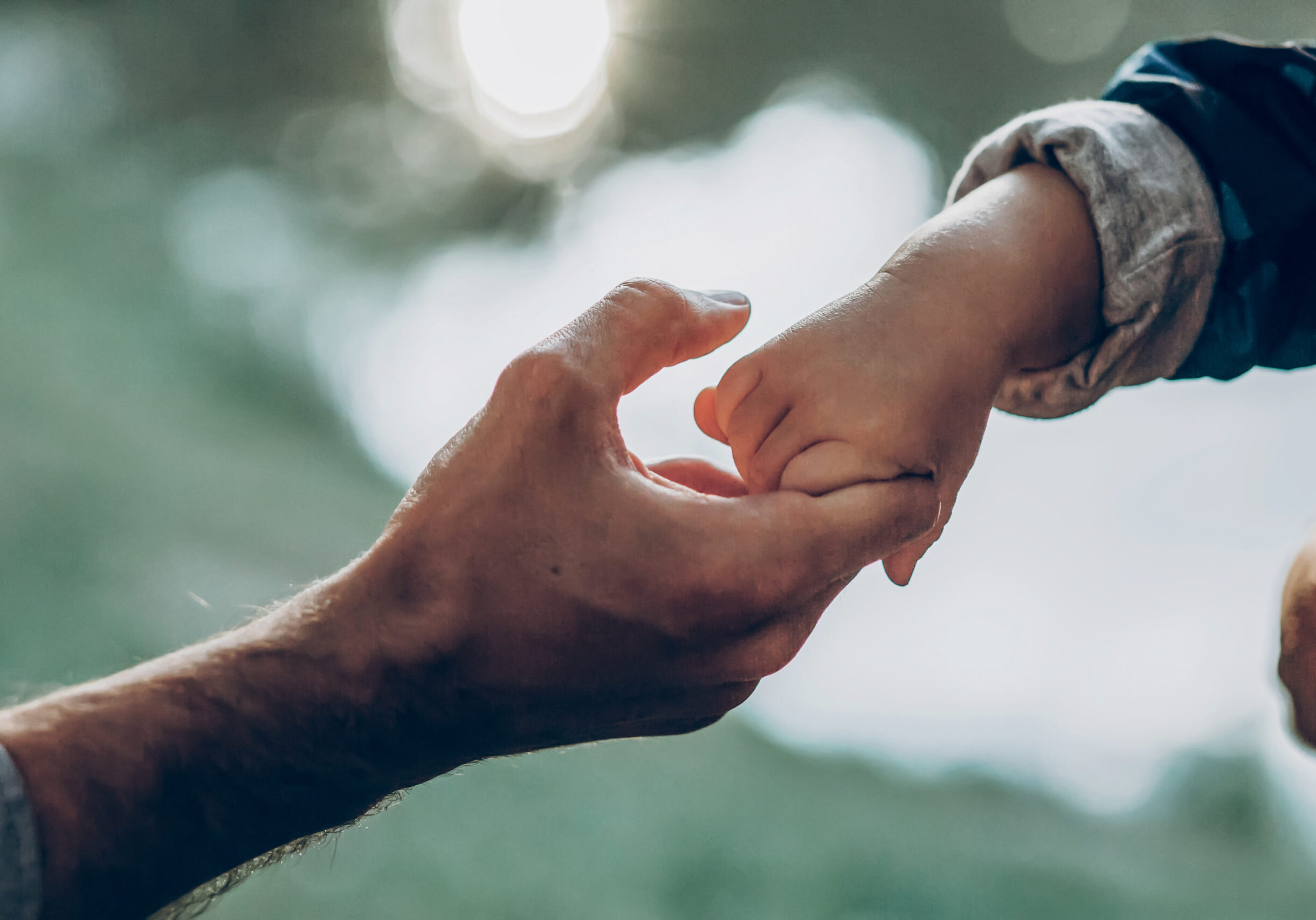 Father and son holding hands outdoors close-up, cute strong dad holding child's arm, parenting and trust concept